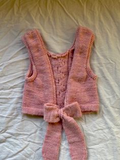 a pink knitted sweater with a bow on the front and back, laying on a bed