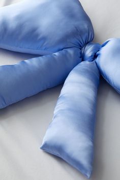 two blue pillows on top of a white bed with a knot at the end of each pillow