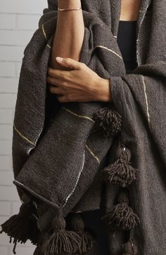 a woman wearing a brown scarf with tassels on the ends and her hands folded over her shoulder