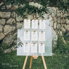 a wooden easer with seating cards on it in front of a stone wall and greenery