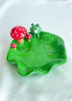 a frog sitting on top of a green leafy plant with a toad figurine next to it