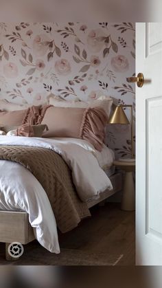 a bedroom with pink and white floral wallpaper on the headboard, bedding and pillows