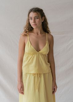 Brighten your days with our Mökki Halter Top in Sunlight, a dreamy pastel yellow that radiates joy. Hand-dyed by artisans in Bali, each top is unique, showcasing the beauty of its creation. Made from soft, breathable Cotton Slub, this top is perfect for embracing the warmth of summer. This feminine halter top features adjustable multifunctional straps for effortless elegance, which can be tied around the neck or attached to two hidden loops at the back, allowing you to style it any way you choos Yellow V-neck Top For Loungewear, Yellow Linen Summer Tops, Natural Dye Tops For Spring Beach, Yellow Summer Tops For Loungewear, Yellow Summer Top For Daywear, Yellow Summer Tops For Daywear, Yellow Linen Tops For Spring, Yoga Flare Pants, Bra Cup