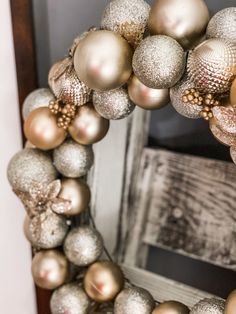 a wreath made out of christmas balls on top of a wooden frame with an old door in the background