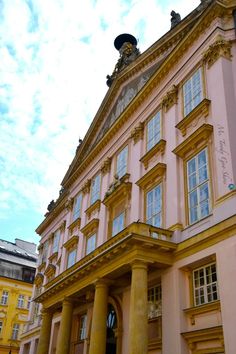 an old pink building with columns on the front and side, under a cloudy blue sky