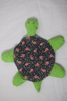 a green stuffed turtle with roses on it's shell sitting on a white sheet