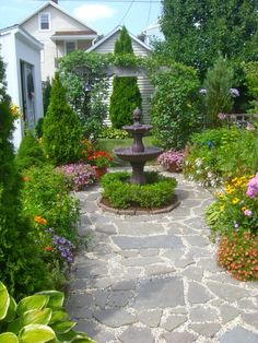 a garden with lots of flowers and plants around it in front of a white house