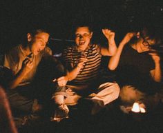 four people sitting around a campfire with one person holding his hand up in the air