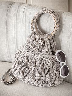 a crocheted purse sitting on top of a couch next to sunglasses and a chain