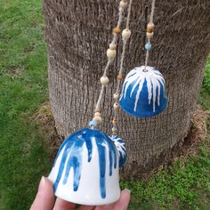 a hand holding a blue and white ceramic bell ornament next to a tree