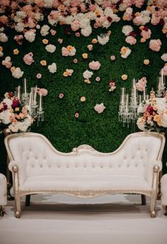 a white couch sitting in front of a lush green wall with flowers on it's side