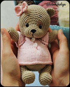 a crocheted teddy bear in a pink dress is being held by someone's hands