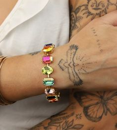 a person with tattoos on their arm holding onto a bracelet that has different colored stones