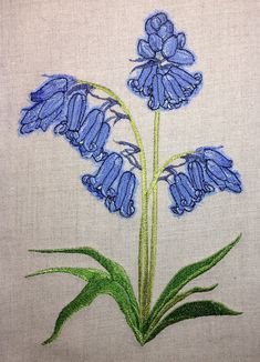 a blue flower with green leaves on a white background is embroidered onto a piece of cloth