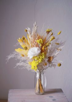 a vase filled with yellow and white flowers on top of a wooden table next to a wall