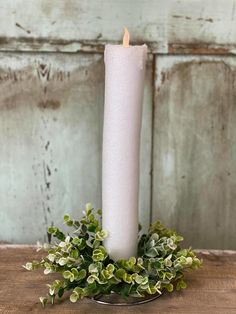 a white candle sitting on top of a wooden table next to some green leaves and greenery