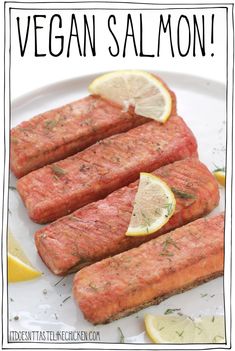 three raw salmon fillets on a white plate with lemons and herbs