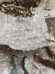 two people standing in front of a stone with the inscription john proctor hanged on it