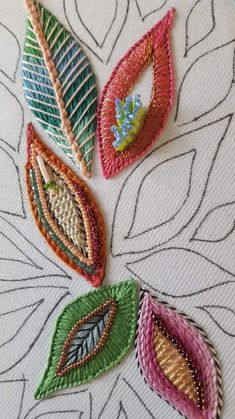 four embroidered leaf designs on a white surface with lines and leaves in the middle, all different colors