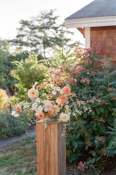 a tall wooden vase filled with flowers on top of a lush green field next to a house