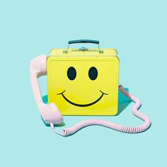 a yellow lunch box with a smiley face on it and a pink phone in the foreground