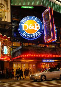 people are walking on the sidewalk in front of a building with neon signs and lights