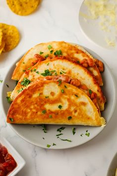 three quesadillas on a plate with salsa and tortillas in the background