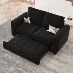 a living room with a black couch and ottoman on the rug in front of it