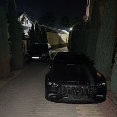 two black cars parked in front of a house at night with the headlights turned on