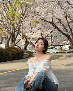 a woman sitting on the ground in front of some trees with pink blossoming flowers