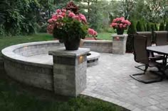 an outdoor patio with table, chairs and fire pit surrounded by flowers in the background