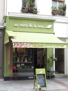 the outside of a flower shop with green awnings and potted plants on display