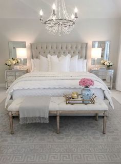 a bedroom with a large white bed, chandelier and two tables in front of it