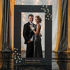 a couple standing next to each other in front of a photo frame with lights on it