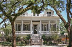 a large white house surrounded by trees on a sunny day