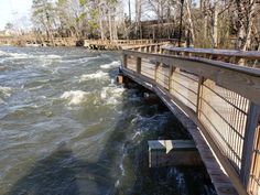 a wooden bridge over a river with rapids on both sides and trees in the background