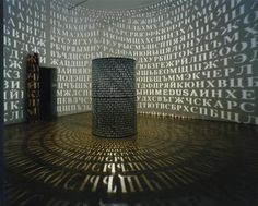 an art installation with many letters projected on the wall and in front of it is a large cylinder