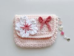 a pink crocheted purse with two white flowers on the front and one red flower on the back