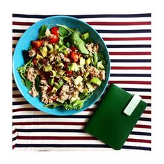 a blue plate topped with salad on top of a striped table cloth next to a green napkin