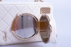 The New 24S Chanel Collectible Runway Camera White Mirror Crossbody Bag Handbag is a standout piece from Chanel's latest collection. This bag features a sleek and compact rectangular shape, designed to be both practical and stylish. Its exterior is crafted from high-quality white leather, which gives it a clean and sophisticated look. The bag is accented with gold-tone hardware, adding a touch of luxury. One of the most distinctive features of this bag is its mirror detail. The lens of the camera-shaped bag opens to reveal a mirror inside, making it both a fashion statement and a functional accessory. The bag has a zip-around closure and a long chain strap, allowing it to be worn comfortably as a crossbody. The interior is lined with soft lambskin, providing a luxurious feel and ensuring t Mirror Detail, White Mirror, Chanel Spring, Functional Accessories, Long Chain, Gold Tone Metal, Chain Strap, White Leather, Fashion Statement