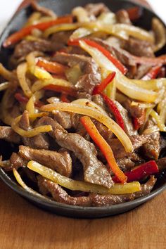 beef and peppers in a skillet on top of a wooden table, ready to be eaten