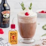 there is a chocolate drink with whipped cream and cherries on the rim next to other ingredients