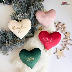 three personalized heart ornaments hanging from a christmas tree with evergreen branches and star ornament