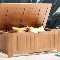 an open wooden chest sitting on top of a white table next to pillows and plants