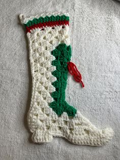 a crocheted christmas stocking is laying on a white blanket with red and green trim