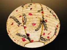 a paper lantern hanging from a ceiling with red flowers and leaves painted on the bottom