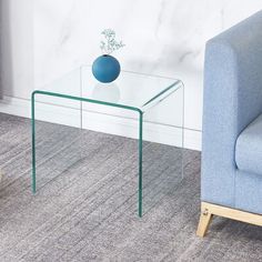 a glass table with a blue vase on it in front of a chair and wall