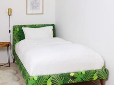 a green bed with white sheets and pillows in a small room next to a chair