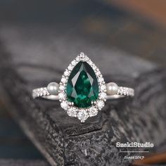 an emerald and pearl ring on top of a piece of wood with pearls around it