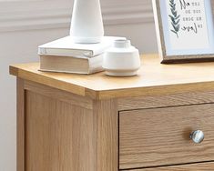 a wooden dresser with two white vases and a framed photo on top of it